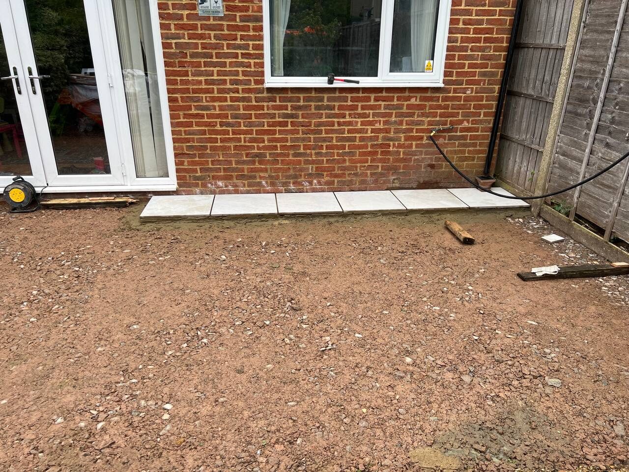 Bare garden ground dug out and levelled with the first row of slabs laid against the house