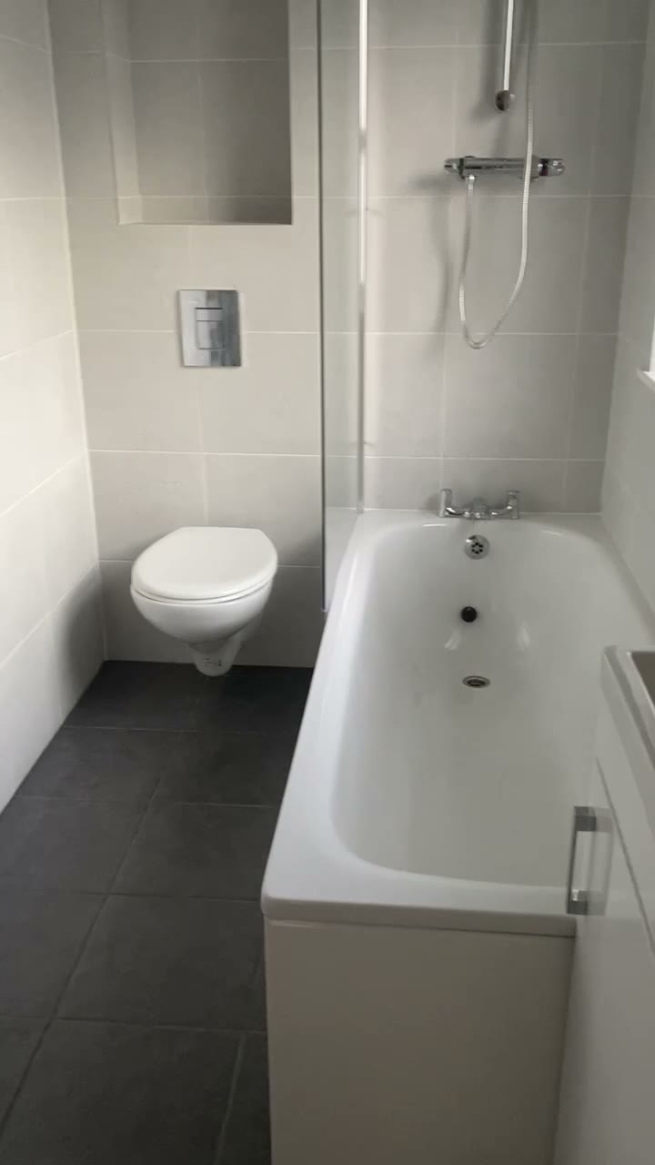 Finished bathroom with wall-hung WC, shower over bath, glass screen and charcoal floor tiles